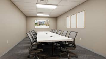 A conference room with a long table, chairs, a carpeted floor, a framed picture on the wall, and a ceiling with recessed lighting.