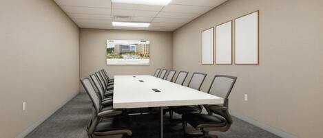 A conference room with a long table, chairs, a carpeted floor, a framed picture on the wall, and a ceiling with recessed lighting.