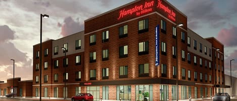 A Hampton Inn by Hilton hotel with a brick facade, multiple windows, and a 'Welcome' sign.