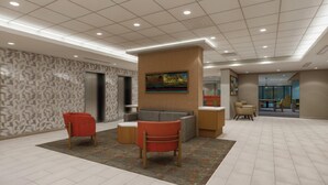 A lobby with a reception desk, two red chairs, a gray sofa, patterned walls, and a ceiling with recessed lighting. - Hampton Inn By Hilton Manhattan Aggieville (Manhattan)