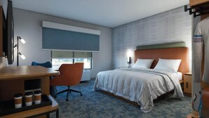A hotel room with a bed, a desk with a chair, a window, and a wall with a textured pattern. - Hampton Inn By Hilton Manhattan Aggieville (Manhattan)