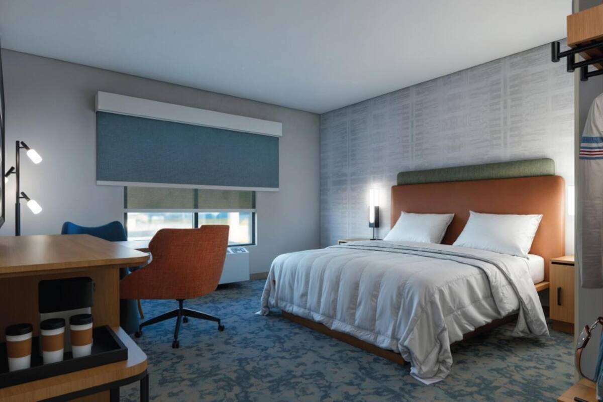 A hotel room with a bed, a desk with a chair, a window, and a wall with a textured pattern.