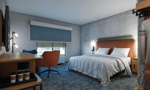 A hotel room with a bed, a desk with a chair, a window, and a wall with a textured pattern. - Hampton Inn By Hilton Manhattan Aggieville (Manhattan)