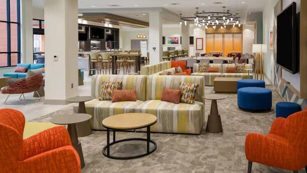 A modern hotel lobby with a central seating area, a bar, and a television screen. - Hilton Garden Inn Oakland Airport Alameda (Alameda)