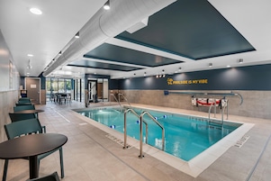 Un área de piscina interior moderna con carriles delimitados, una estación de salvavidas y un espacio de descanso con mesas y sillas.
