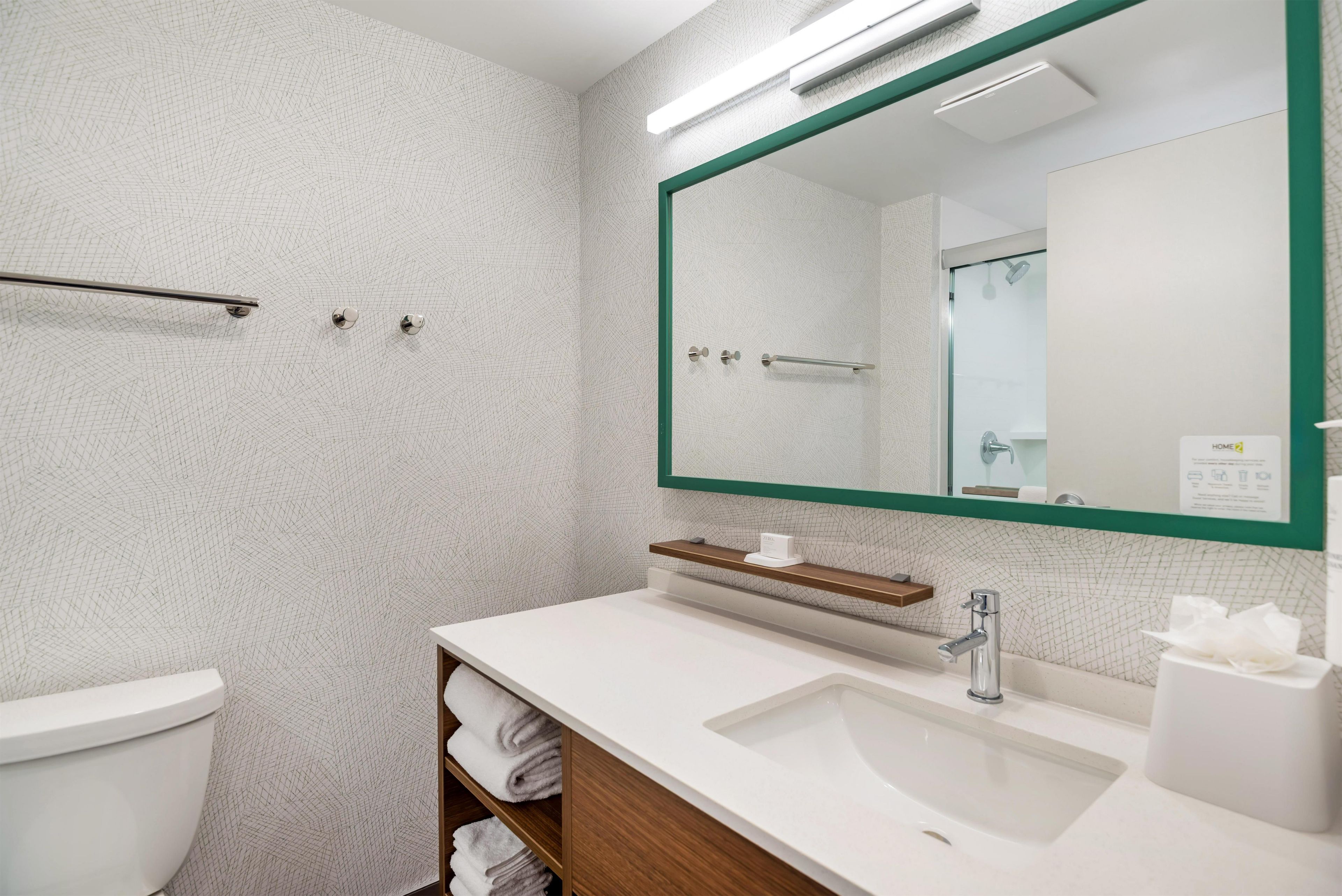 A modern bathroom with a white sink, a mirror with a green frame, and a towel rack.