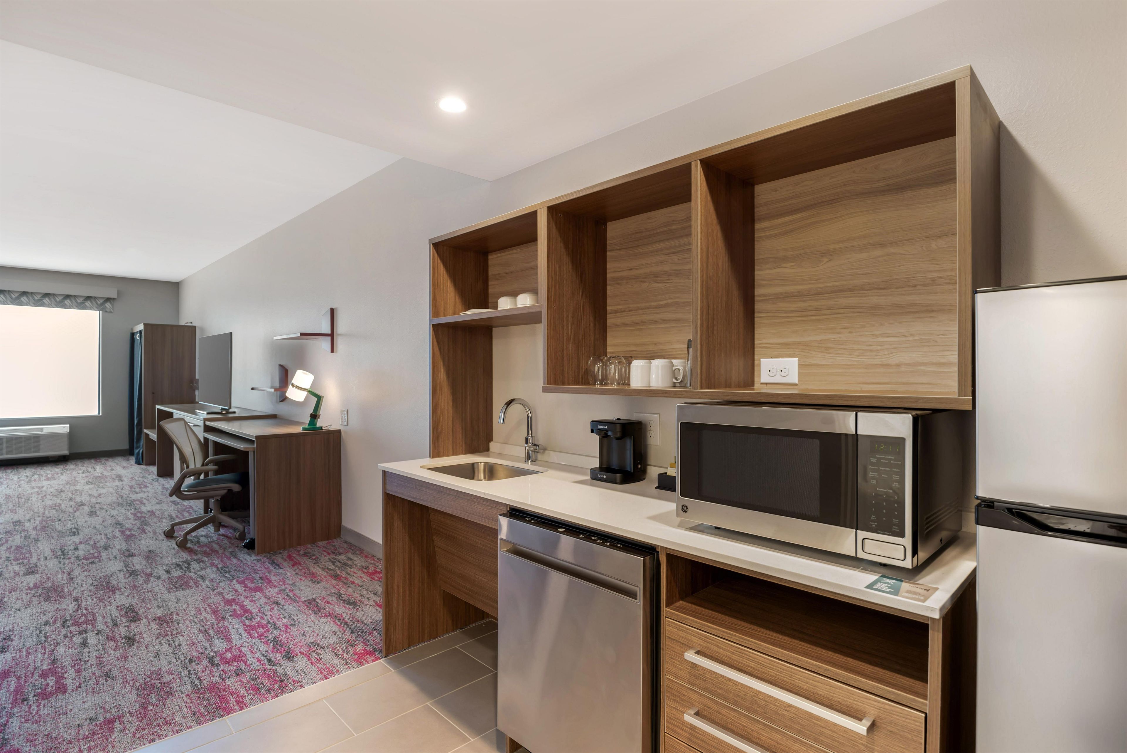 A modern kitchen with built-in appliances, a dining area with a desk and chair, and a large window.