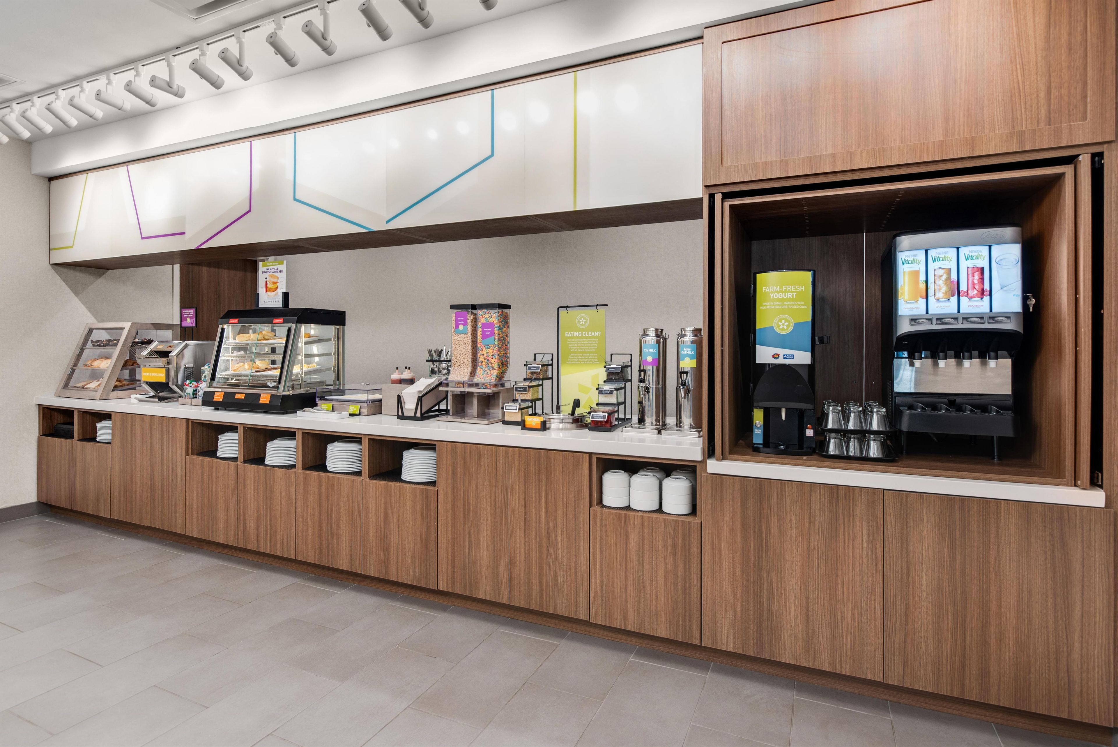 A self-service breakfast area with a coffee machine, yogurt dispenser, and various food items.