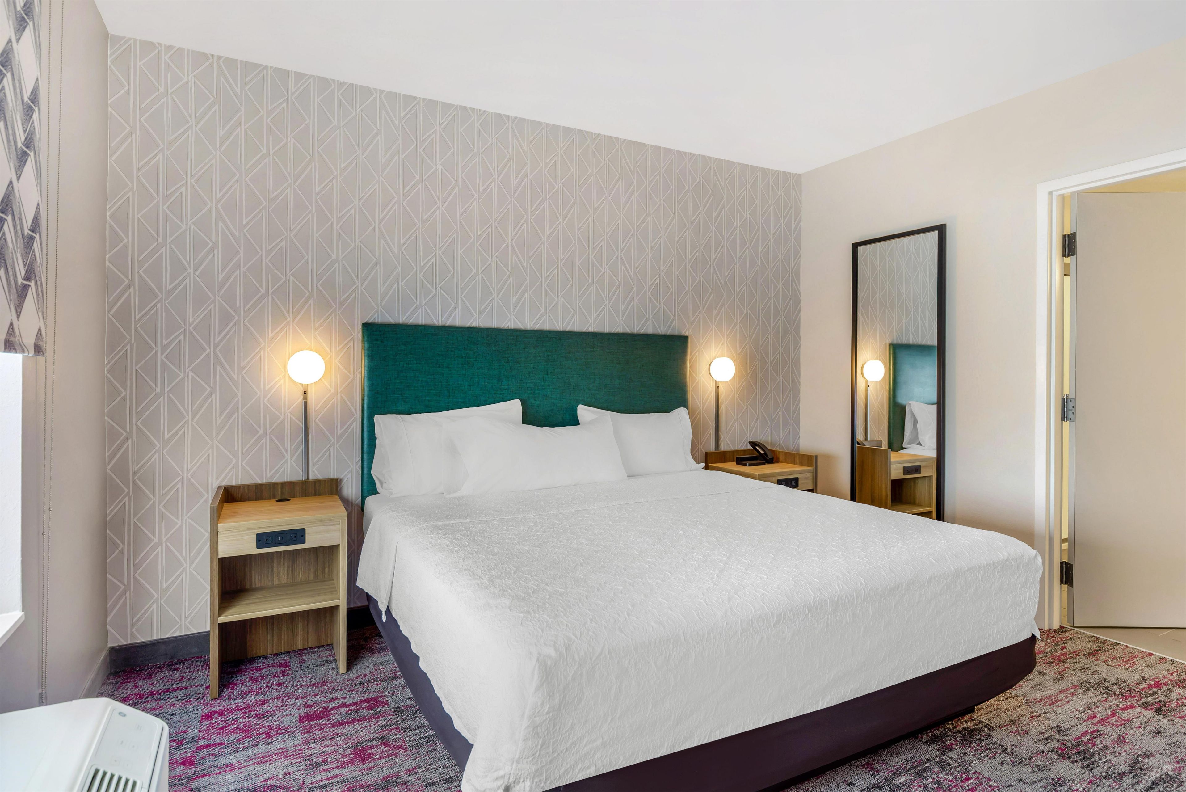 A hotel room with a large bed, two bedside tables, a mirror, and a patterned wall.
