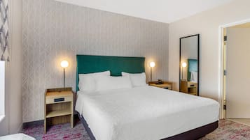 A hotel room with a large bed, two bedside tables, a mirror, and a patterned wall.