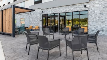 Un espace extérieur aménagé avec des chaises et des tables en osier, une pergola en bois et un mur en pierre.