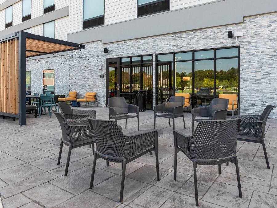An outdoor seating area with wicker chairs and tables, a wooden pergola, and a stone wall.