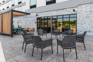 An outdoor seating area with wicker chairs and tables, a wooden pergola, and a stone wall.