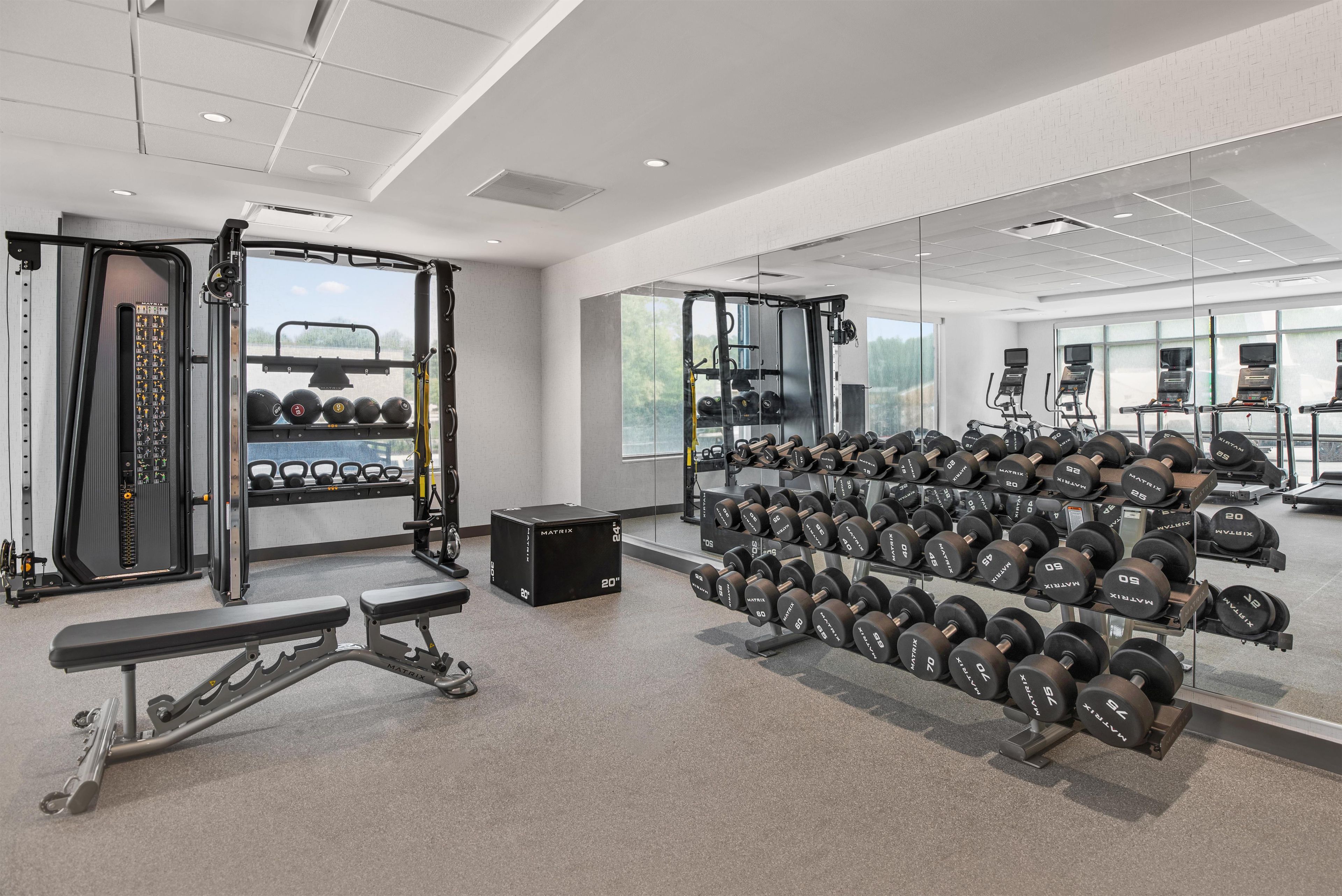 Un gimnasio moderno con equipos de levantamiento de pesas, cintas de correr y un espejo grande.