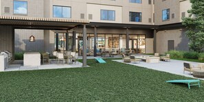 A modern outdoor seating area with tables and chairs, a grassy lawn, and a building with large windows in the background. - Homewood Suites By Hilton Shreveport South (Shreveport)