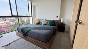 A bedroom with a large window, a bed, a bedside table, and a door. - Livify (Zapopan)