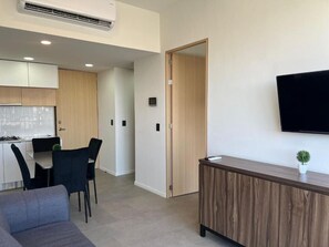 A modern living room with a sofa, a dining table with chairs, a kitchen area, a wooden cabinet, and a mounted TV. - Livify (Zapopan)