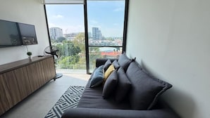 A modern living room with a sofa, a TV, and a balcony with a city view. - Livify (Zapopan)
