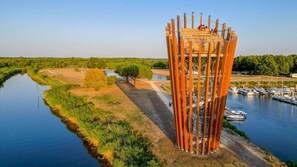 Ein markantes Turmgebäude mit Aussichtsplattform, umgeben von einem ruhigen Fluss und viel Grün.