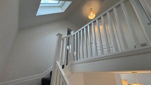 Un escalier avec un puits de lumière, des rampes blanches et une porte en bas.