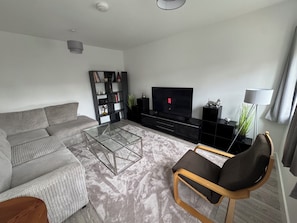 A modern living room with a sofa, a glass coffee table, a TV, a bookshelf, and a floor lamp.