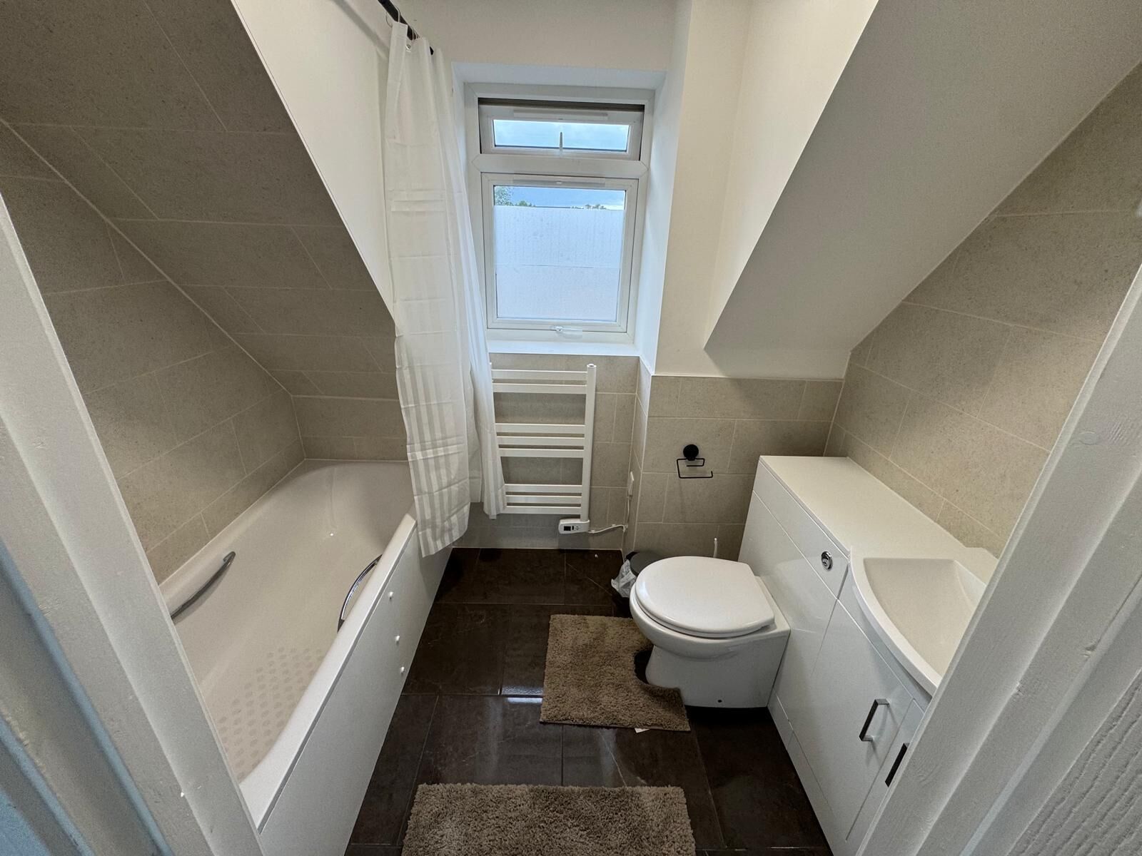 Une petite salle de bain moderne, équipée d’une baignoire, de toilettes et d’une fenêtre.