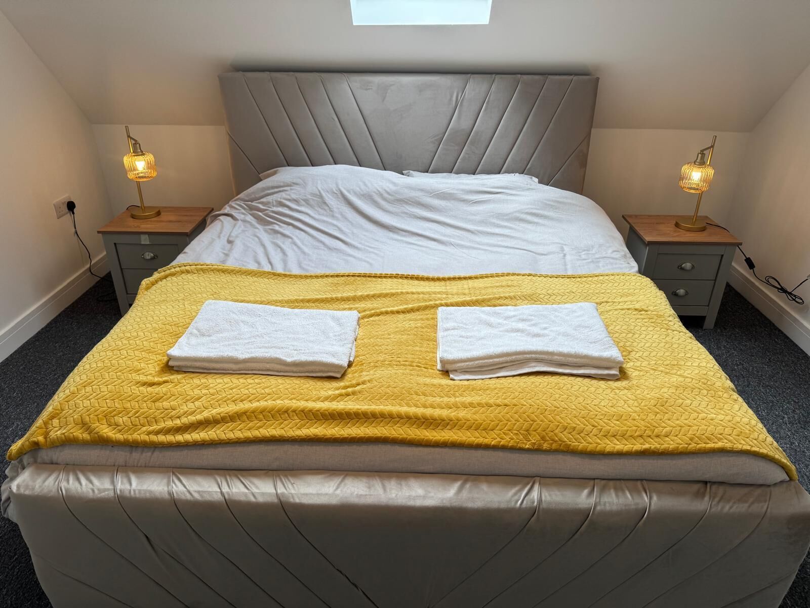 A neatly made bed with a headboard, two bedside tables with lamps, and a yellow blanket.