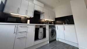 Une cuisine moderne avec des meubles blancs, un puits de lumière, un four encastré, un lave-linge et une machine à café.