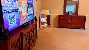 A television displaying a game, a wooden cabinet, a mirror, and a dresser in a room with beige walls. - Welcome to Mr. T's Palace!
Stay big. Relax easy. 
Your Home away from Home. (Jonesboro)