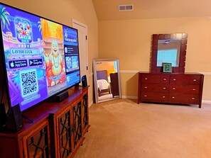 Ein Fernseher zeigt ein Spiel, ein Holzschrank, ein Spiegel und eine Kommode in einem Raum mit beigen Wänden.