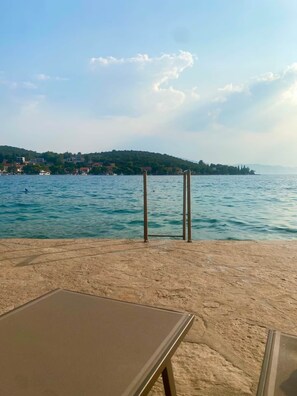 Ein Strand mit Sandbereich, einem Metalltisch und Blick auf das Meer und ferne Hügel.