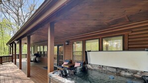 A wooden deck with a hot tub, covered seating, and large windows.