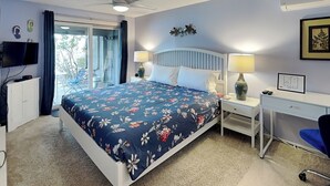 Un dormitorio con una cama, un escritorio, una silla, un ventilador de techo y un televisor.
