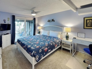 A bedroom with a bed, a desk, a chair, a ceiling fan, and a TV.