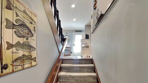 Una escalera alfombrada con barandilla de madera que lleva a una habitación con una puerta y una estantería blanca.