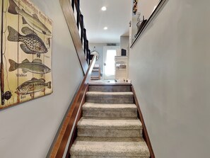 A carpeted staircase with a wooden handrail, leading to a room with a white door and a white shelf unit. - Lakeview Retreat (Oakland)