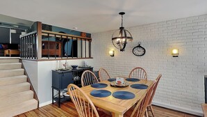 Un comedor con una mesa y sillas de madera, una escalera y una zona de cocina con encimera negra y armarios de madera.