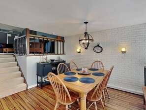 A dining area with a wooden table and chairs, a staircase, and a kitchen area with a black countertop and wooden cabinets. - Lakeview Retreat (Oakland)