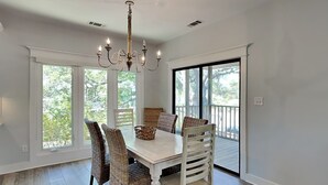 A dining room with a white table, wicker chairs, and a chandelier. - Tybee Straits 17 (Tybee Island)