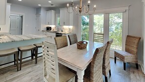 A spacious kitchen with white cabinetry, a central island, and a dining area with wicker chairs and a wooden table. - Tybee Straits 17 (Tybee Island)