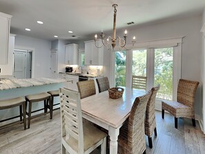 A spacious kitchen with white cabinetry, a central island, and a dining area with wicker chairs and a wooden table. - Tybee Straits 17 (Tybee Island)