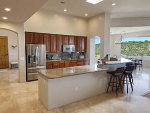 A modern kitchen with wooden cabinets, stainless steel appliances, and a large island with bar stools. - Foothills Luxury Estate | Pool + Pro Golf Sim | Sleeps 12 | Tucson (Tucson)