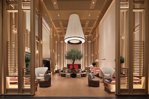 Un hall d’entrée moderne avec un arbre central, des espaces de détente et un grand luminaire au plafond.