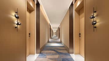 Un pasillo de hotel con suelo alfombrado, paredes de madera y puertas numeradas.
