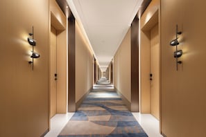 Un couloir d'hôtel avec un sol recouvert de moquette, des murs en bois et des portes numérotées.