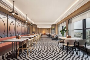 A modern restaurant with high tables, chairs, and a patterned floor. - Hilton Garden Inn Kashgar Ancient City Nanhu (Kashgar)