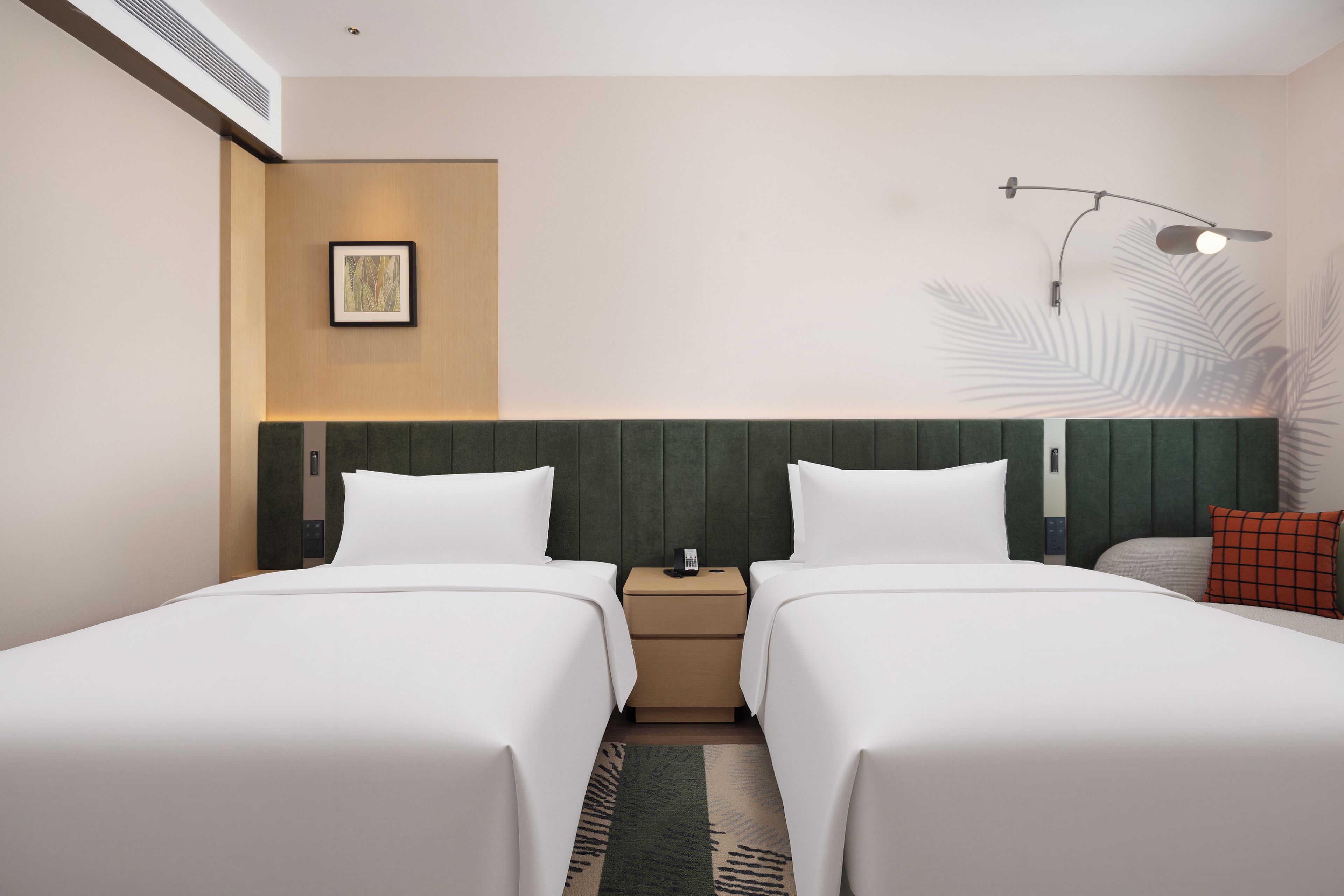 Habitación de hotel con dos camas, una mesita de noche, un teléfono en la pared y un panel decorativo.