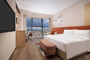 A hotel room with a large window, a bed, a desk, and a chair.