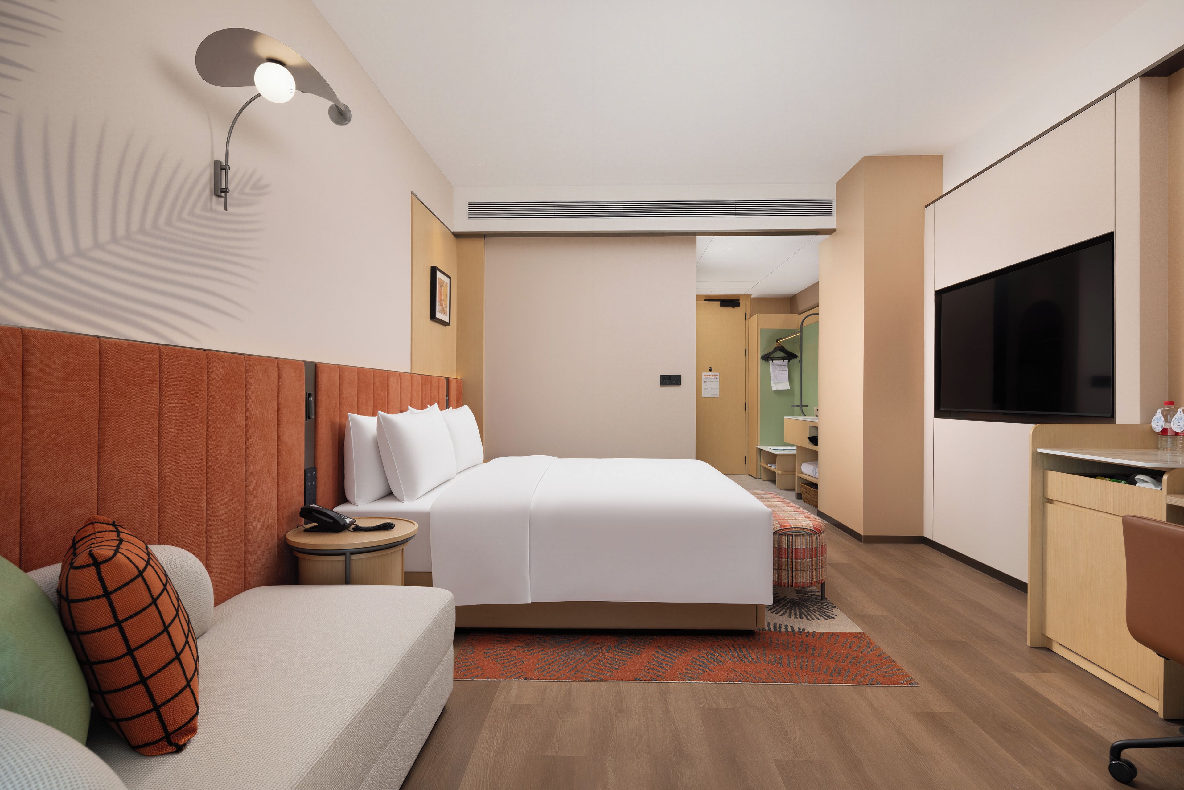 Habitación de hotel con cama, sofá, escritorio, televisión y baño visible a través de una puerta abierta.