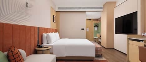 Habitación de hotel con cama, sofá, escritorio, televisión y baño visible a través de una puerta abierta.